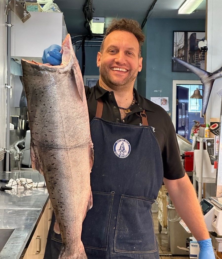 James Heras behind the counter of the family fish market, holding a whole salmon